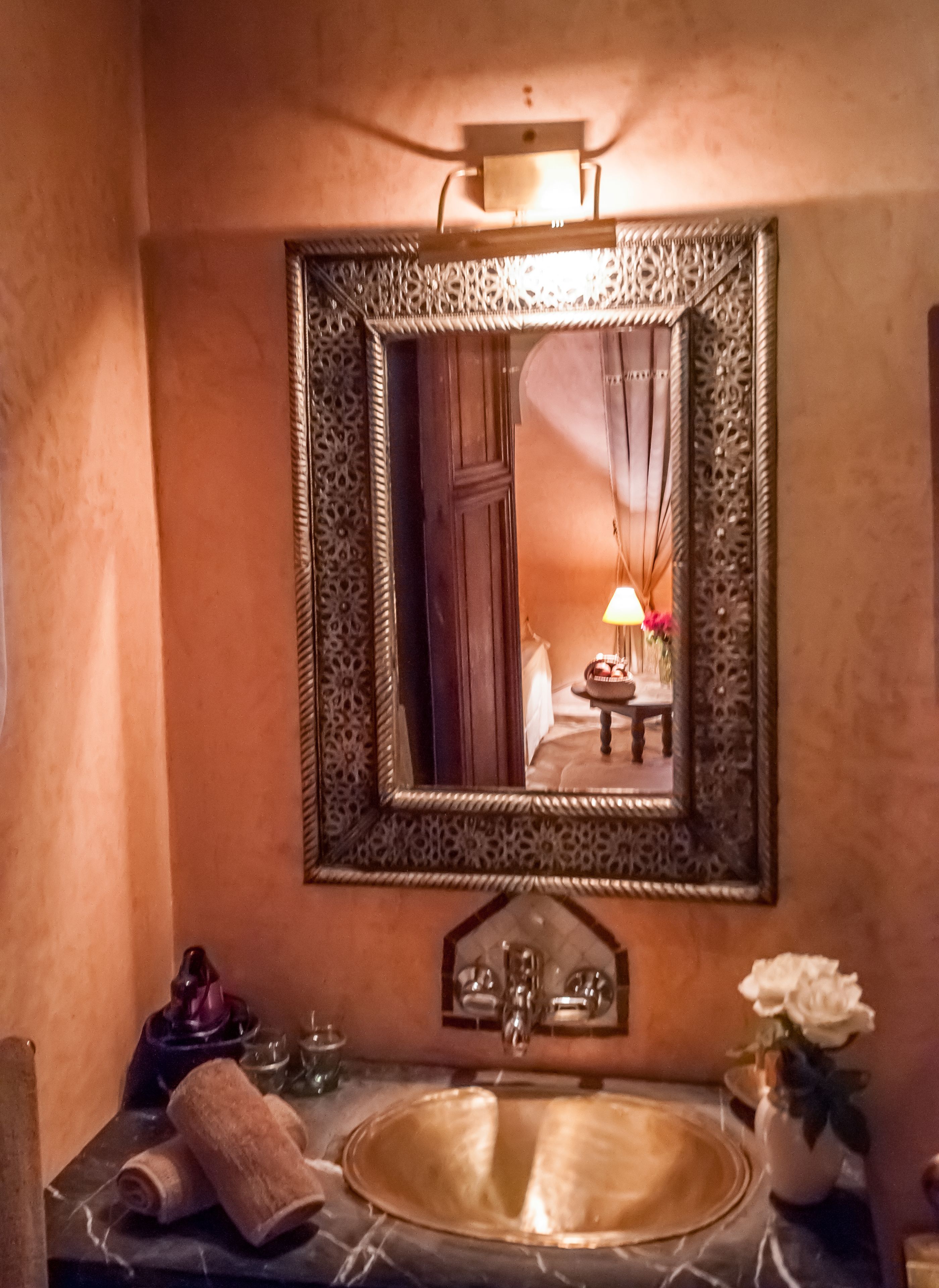 Un bagno con lavabo in marmo, uno specchio decorativo e un vaso con fiori.