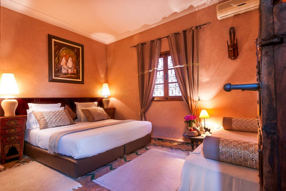 Un dormitorio elegante con una cama grande, una mesita de noche con lámpara, una pequeña mesa con flores y una silla.