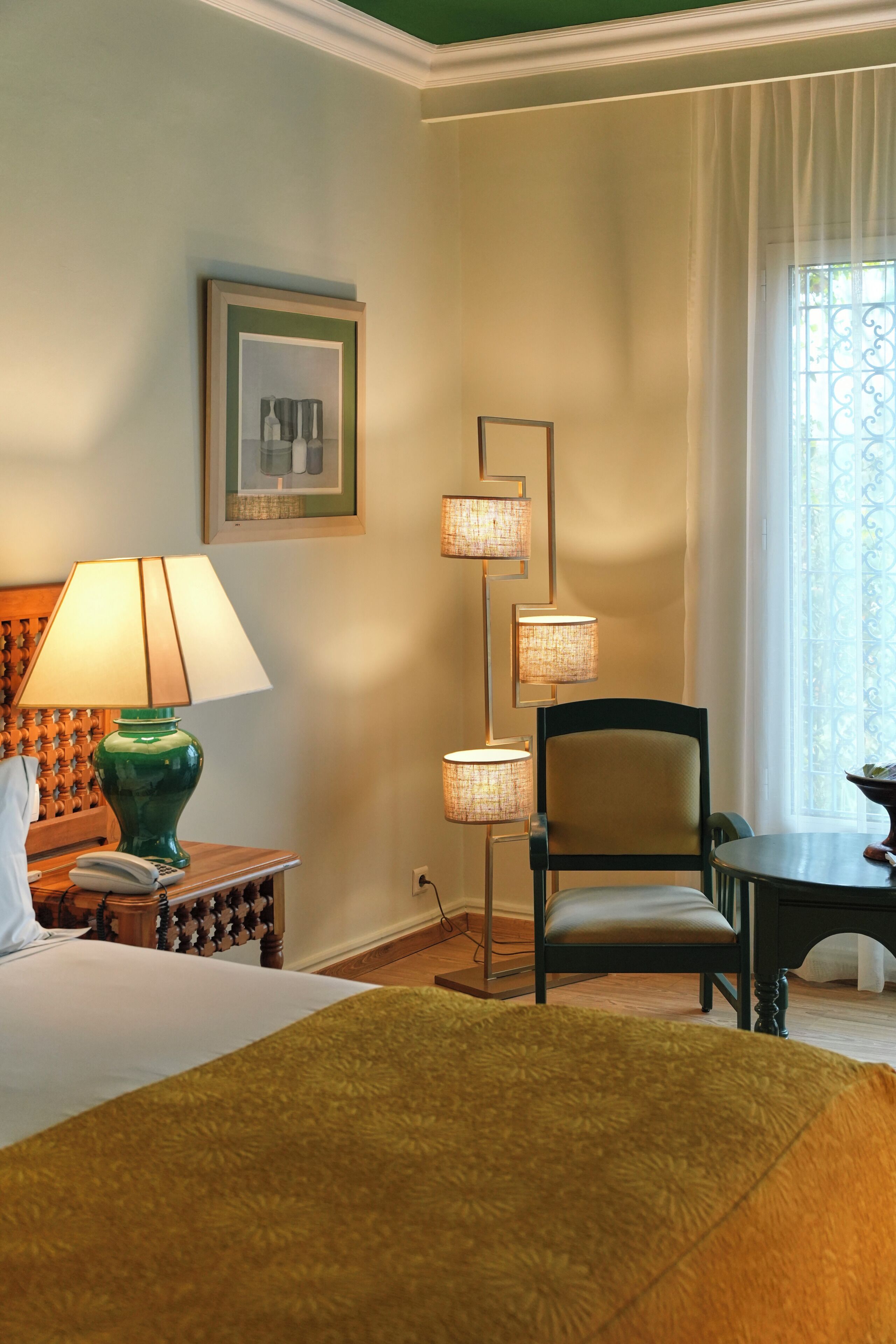 A hotel room with a bed, a chair, a table, a lamp, and a window with curtains.