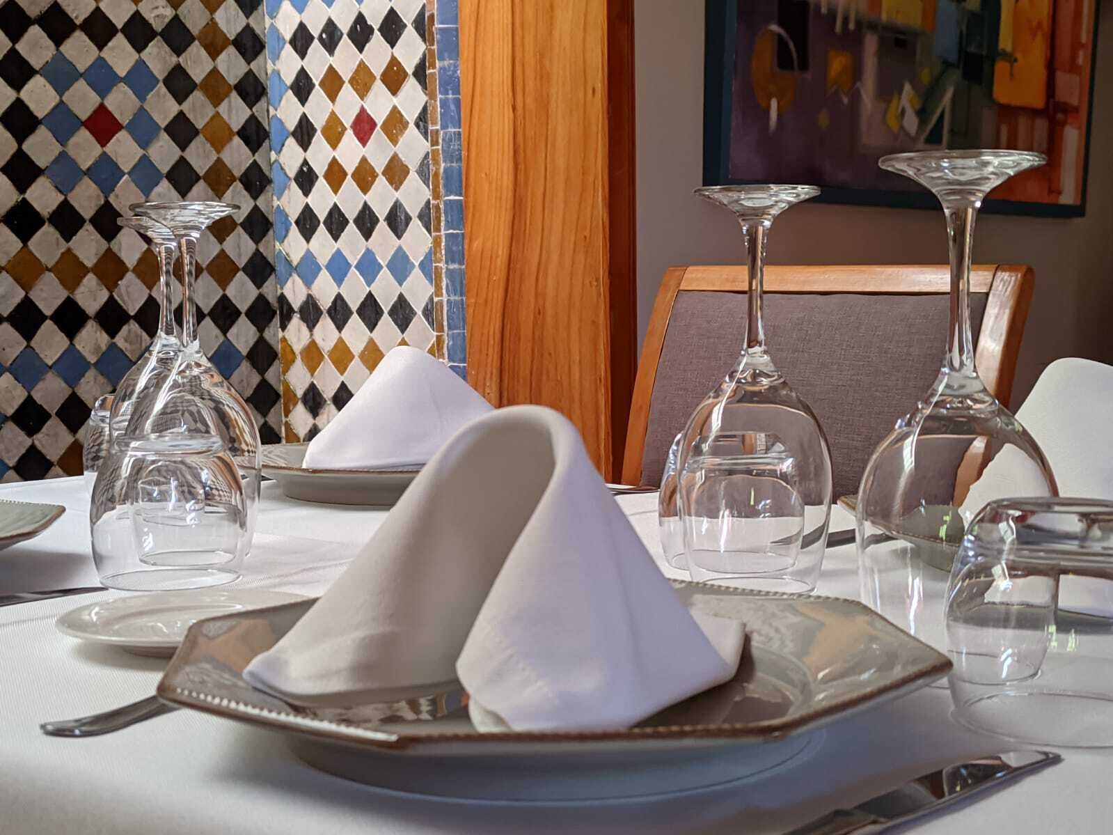 Una mesa de comedor con cristalería transparente, servilletas blancas y un papel tapiz estampado al fondo.
