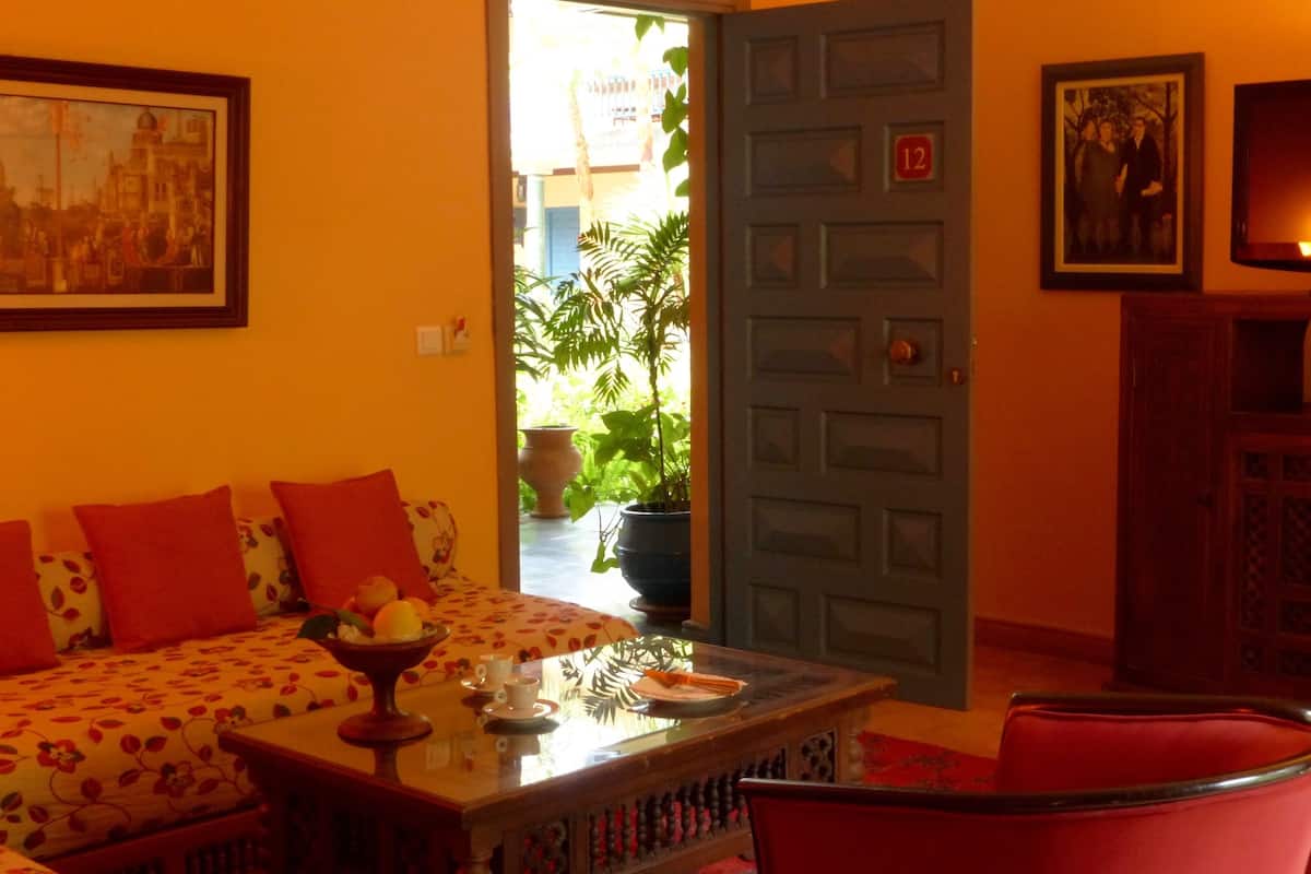 A cozy room with a sofa, a table with a bowl of fruit, and a door leading to a balcony with plants.