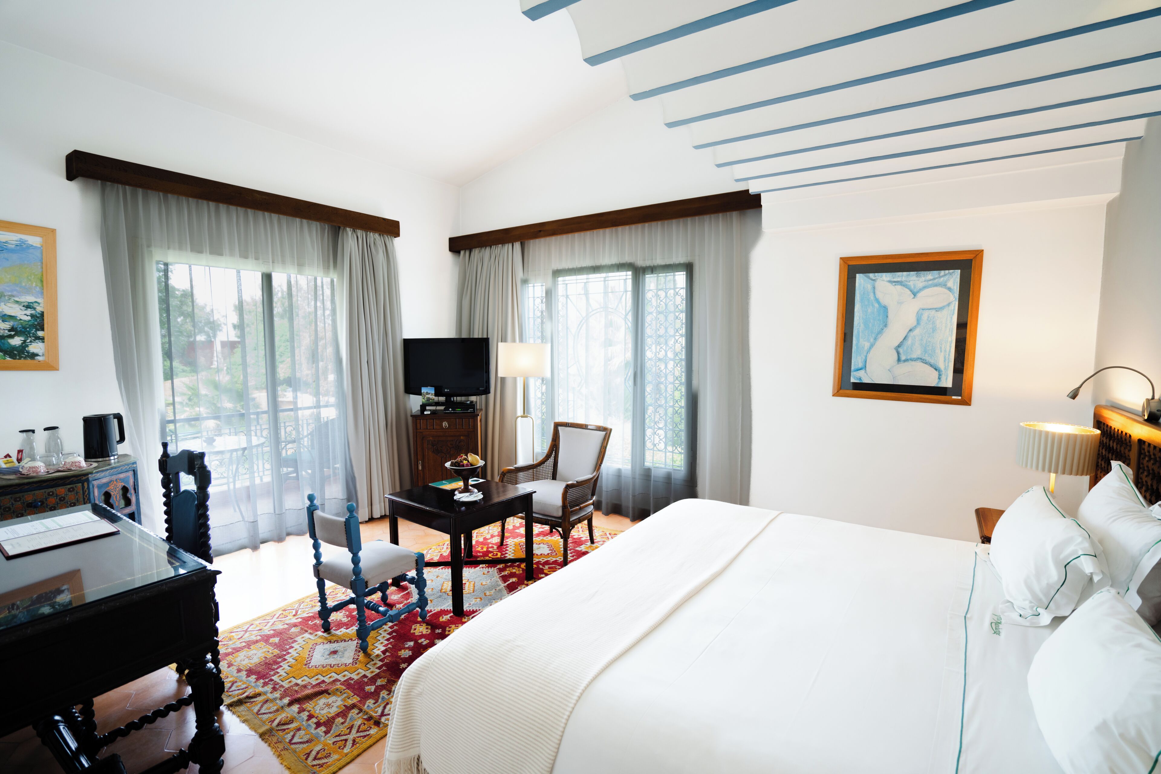 A hotel room with a large bed, a desk with a chair, a television, and a window with curtains.
