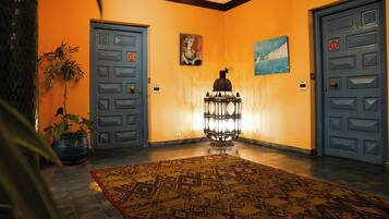 A hallway with two doors, a patterned rug, a potted plant, and wall art.