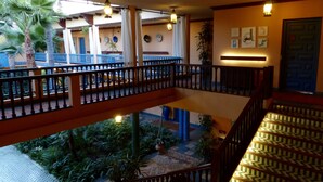 A multi-level indoor area with a wooden railing, a patterned floor, and a view of a courtyard with plants and a palm tree.