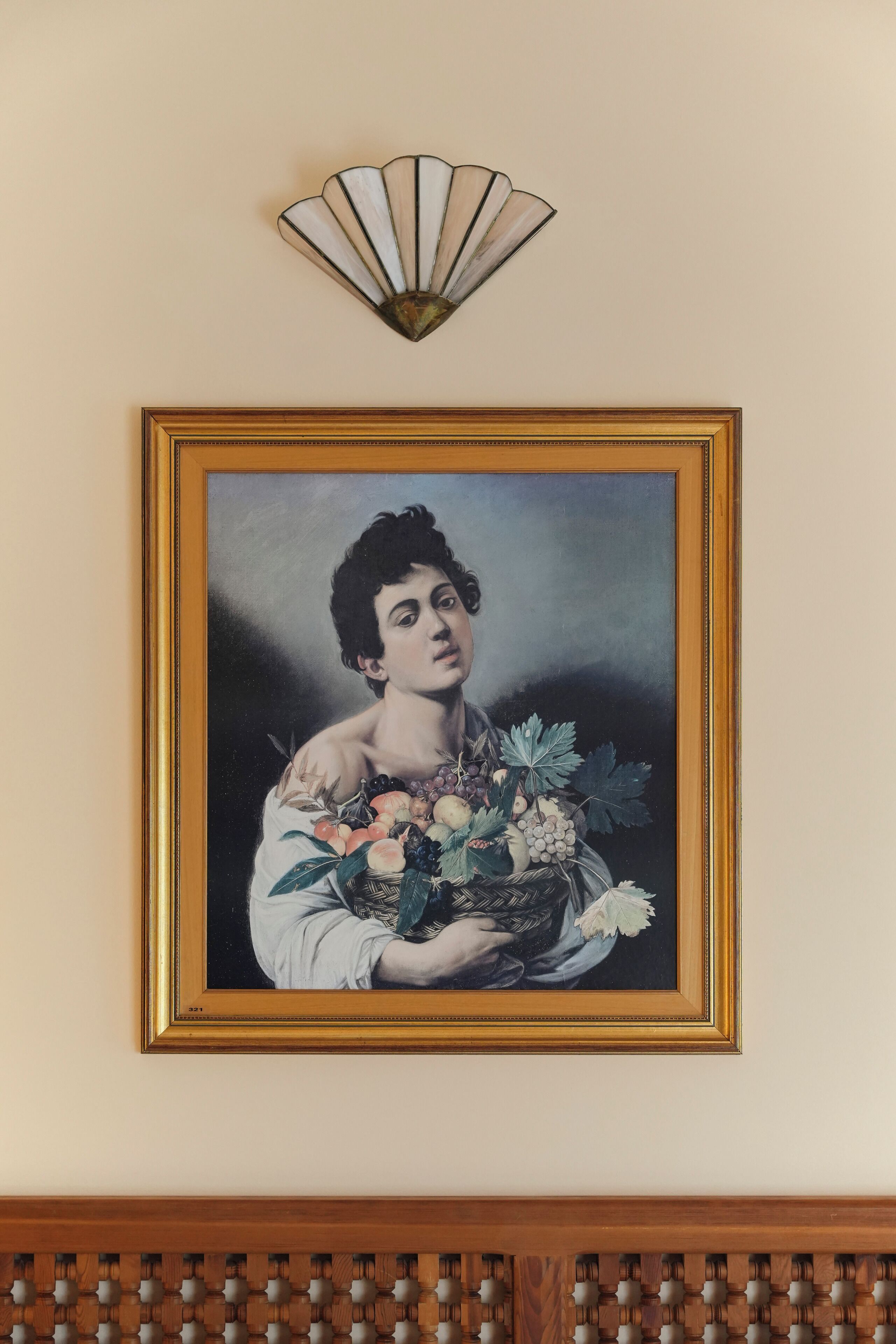 Un retrato enmarco de una persona sosteniendo una cesta de frutas y flores, con un abanico decorativo encima.