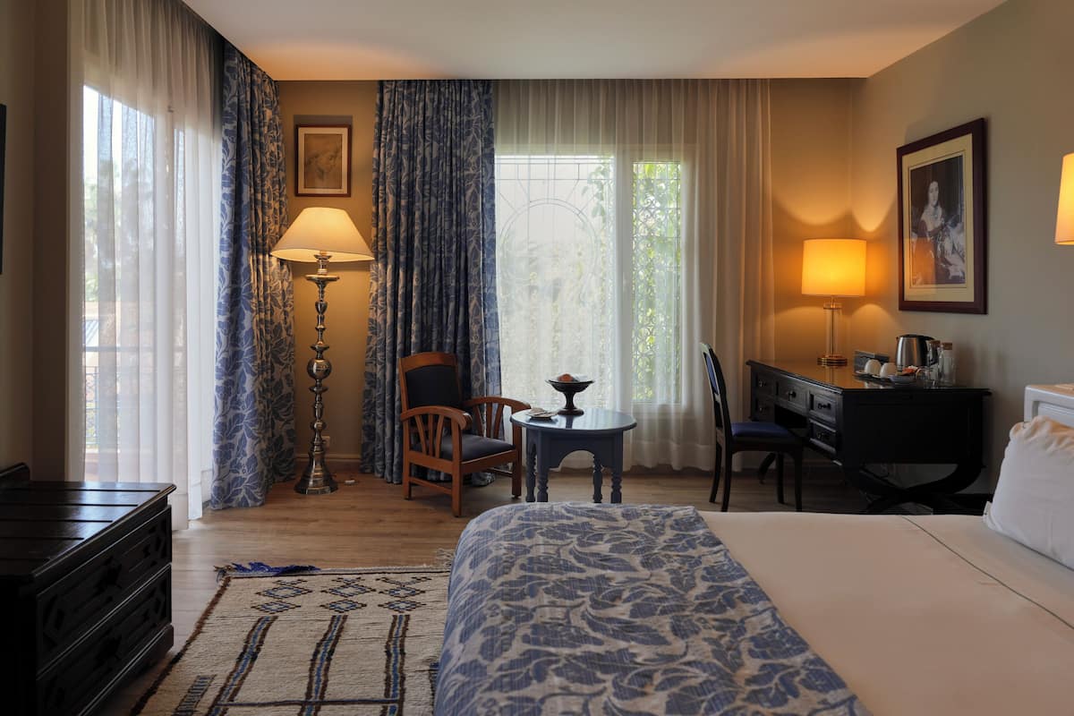 A hotel room with a bed, a desk, a chair, a lamp, and a view of the outdoors.