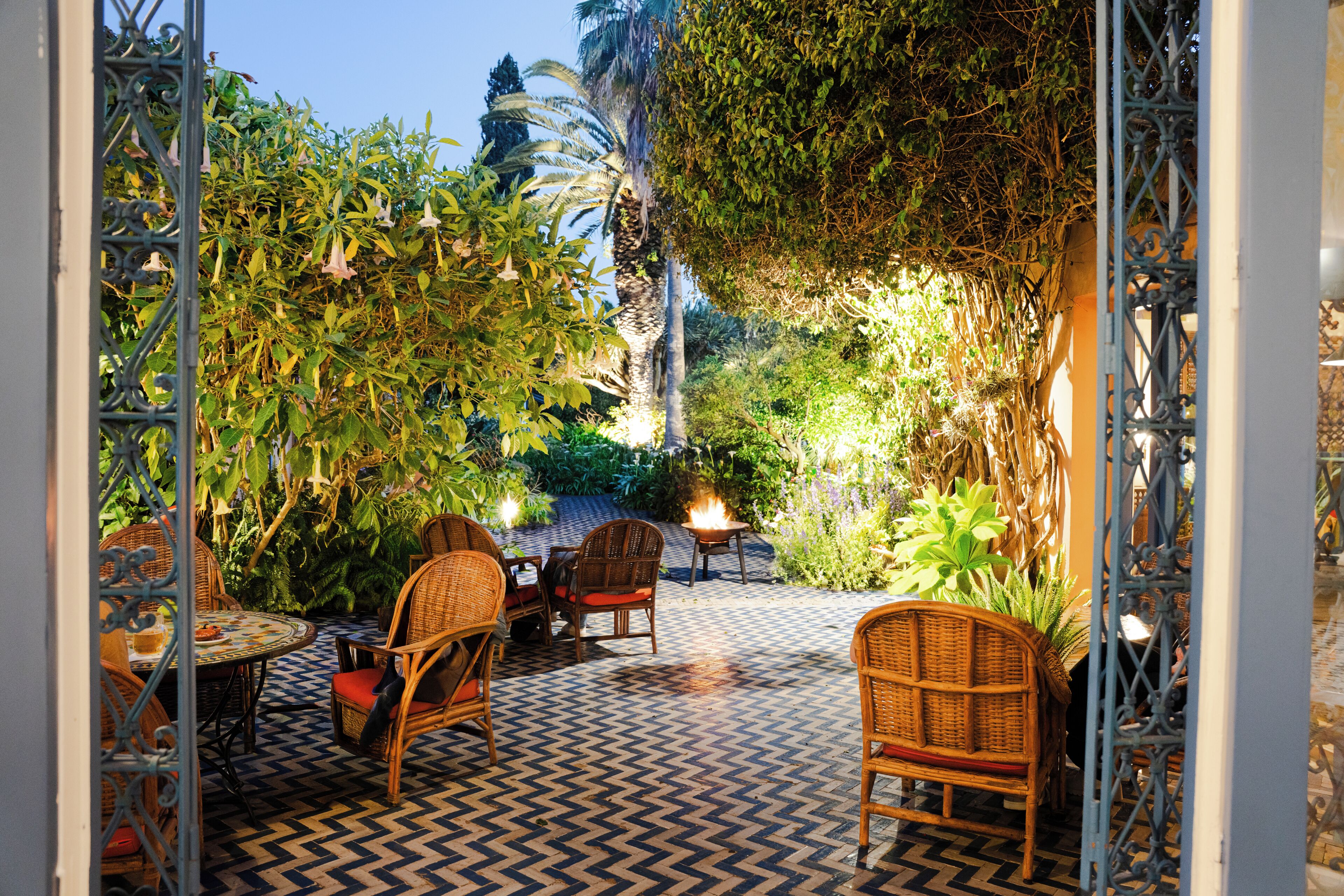 Une terrasse extérieure aménagée avec des meubles en osier, un sol à motifs et une végétation luxuriante.