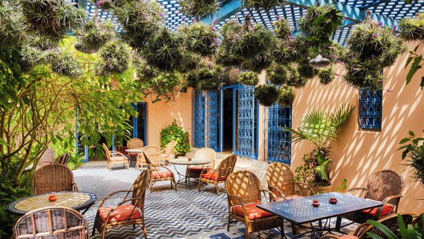 An outdoor patio with wicker furniture, a tiled floor, and hanging plants.
