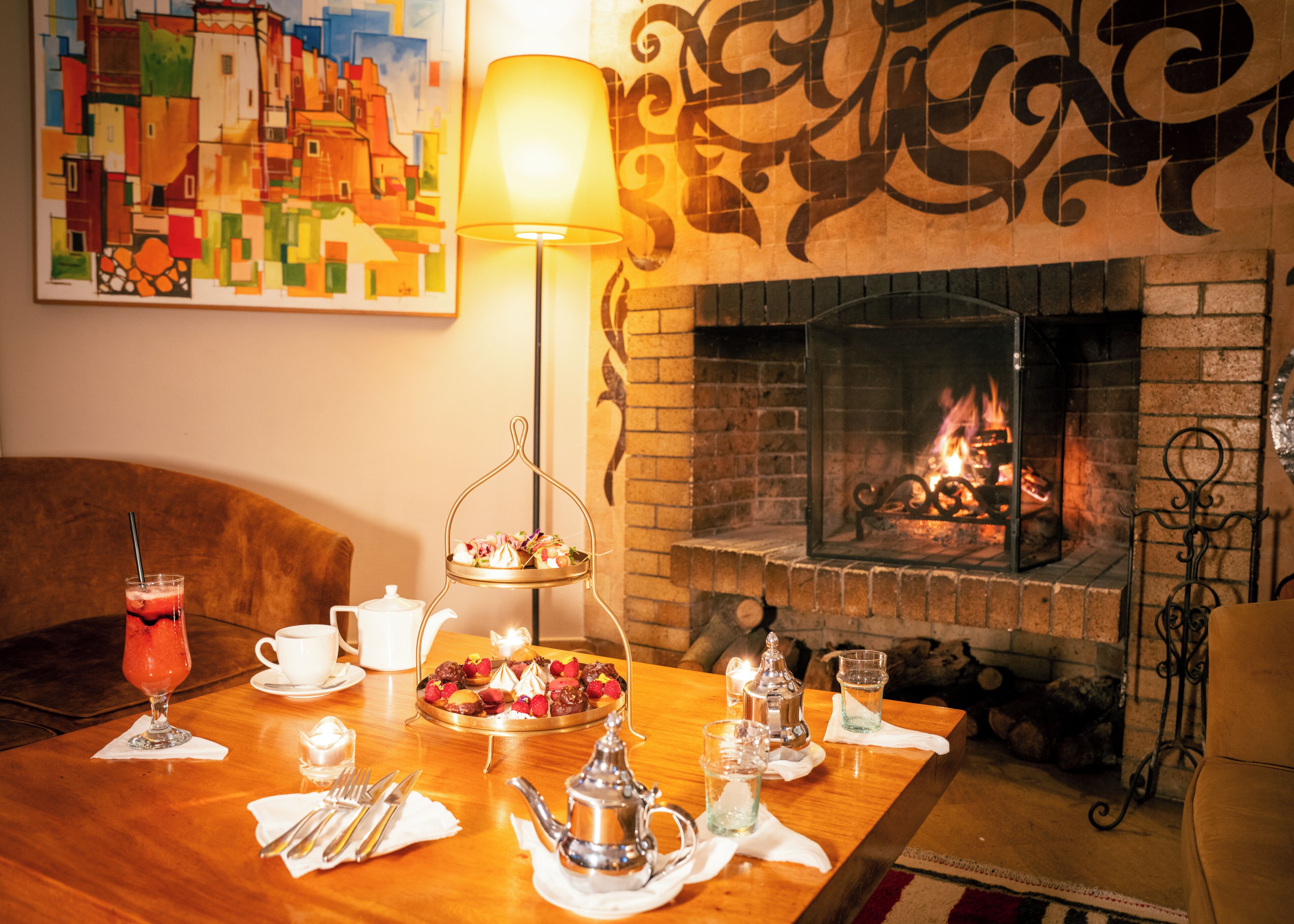 Een knus vertrek met een open haard, een eettafel gedekt met thee servies, en een schilderij aan de muur.