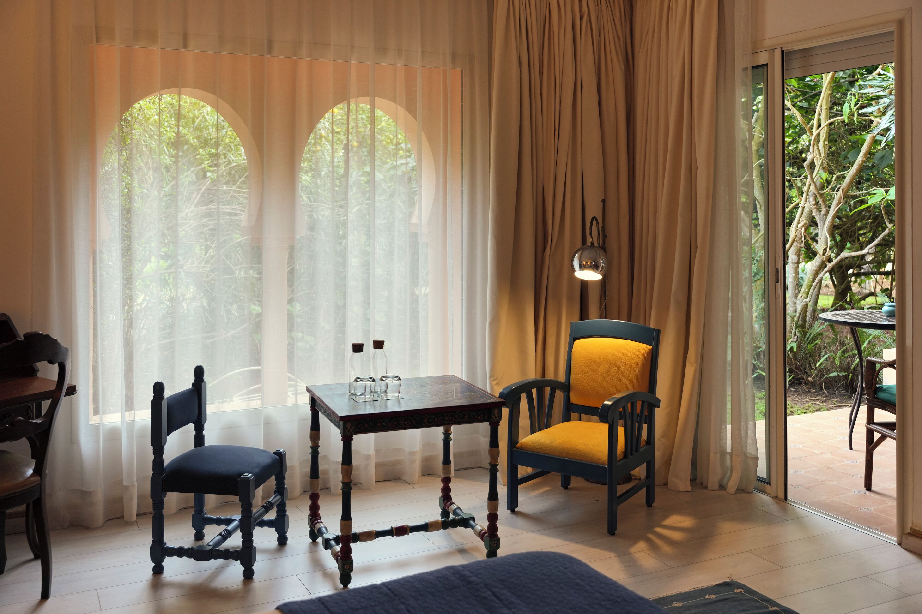 A room with a table, two chairs, a lamp, and a view through a window.