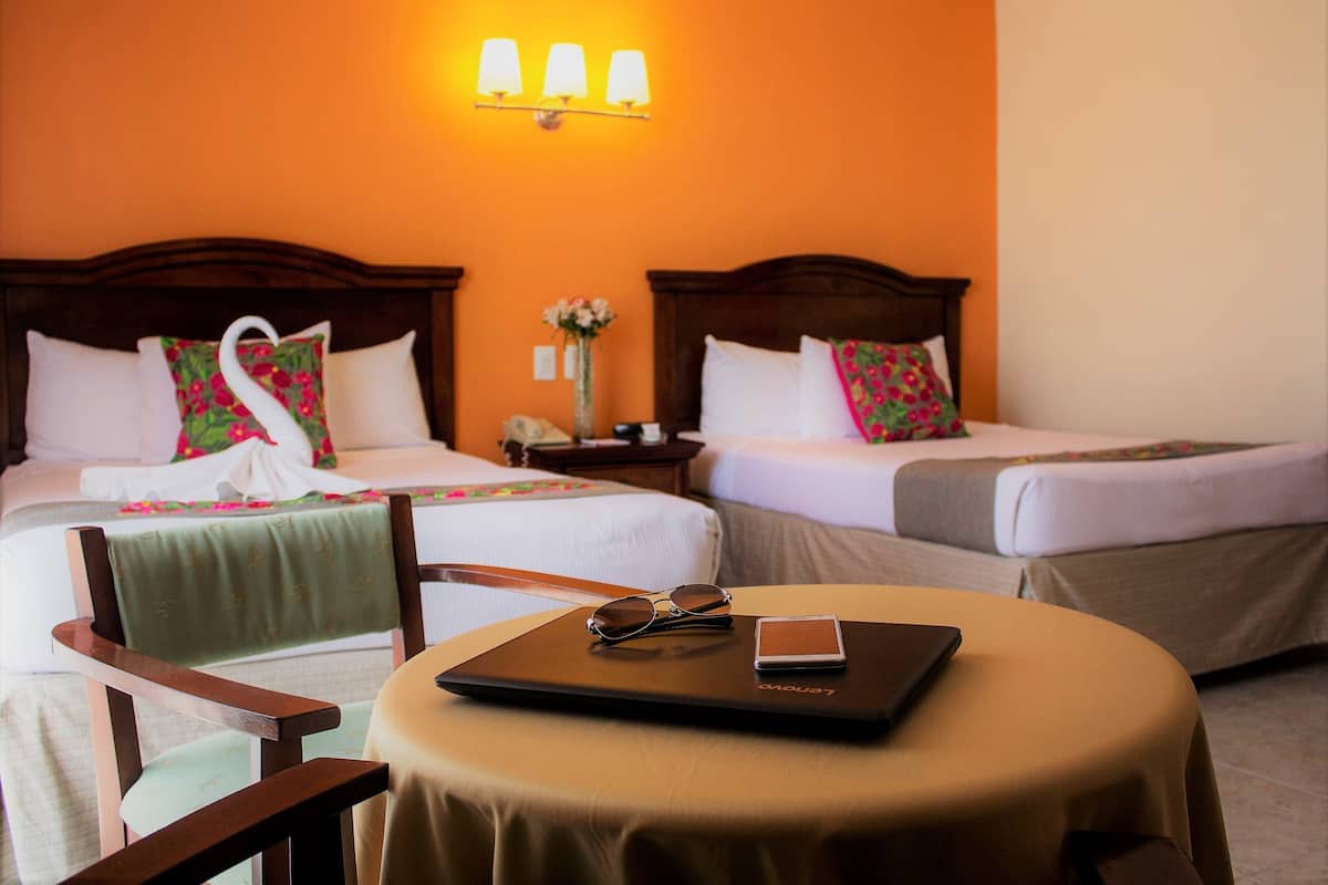 Een hotelkamer met twee bedden, een ronde tafel met een laptop en zonnebril, en een stoel.