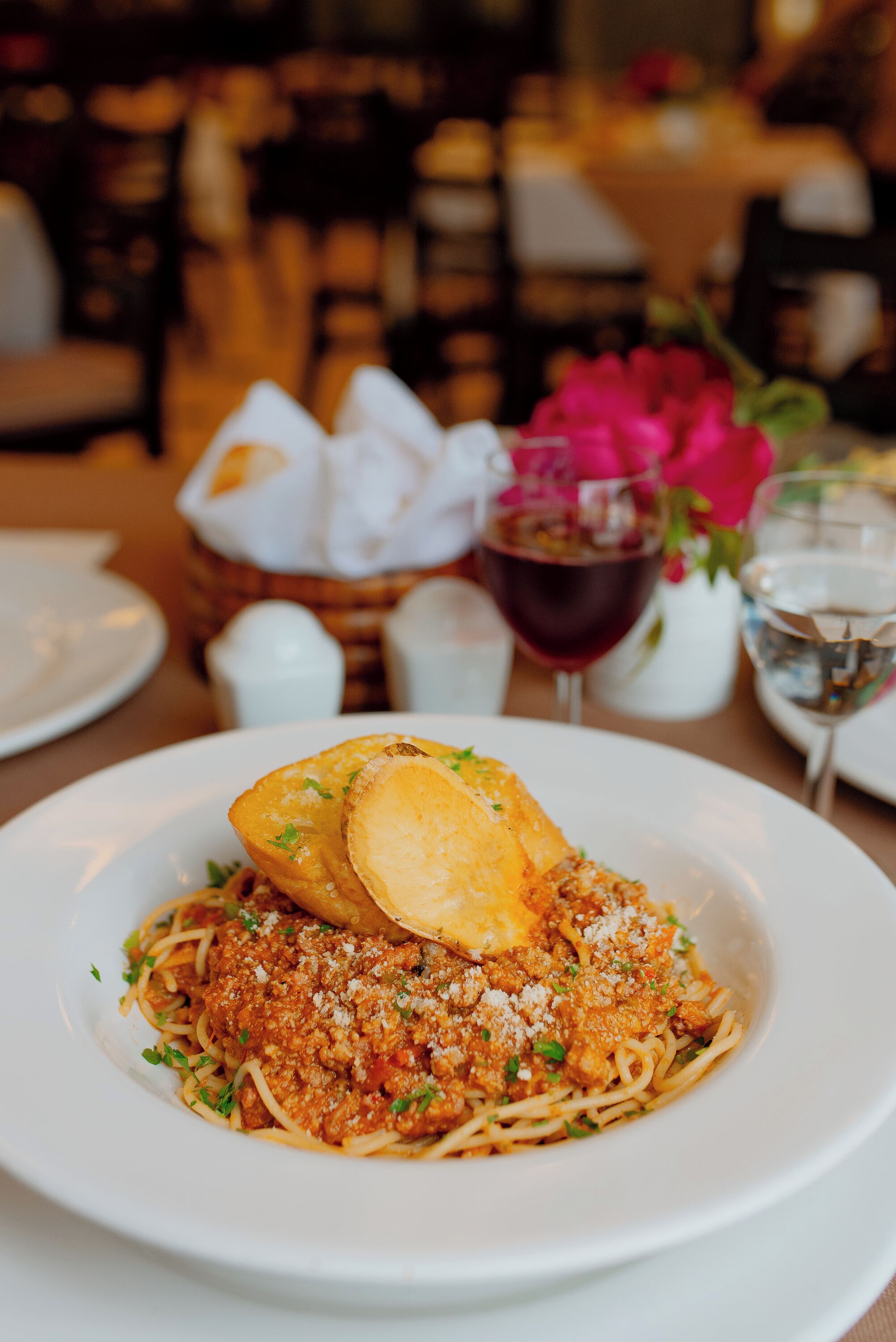 A plate of spaghetti with meat sauce and a slice of bread on a white plate.
