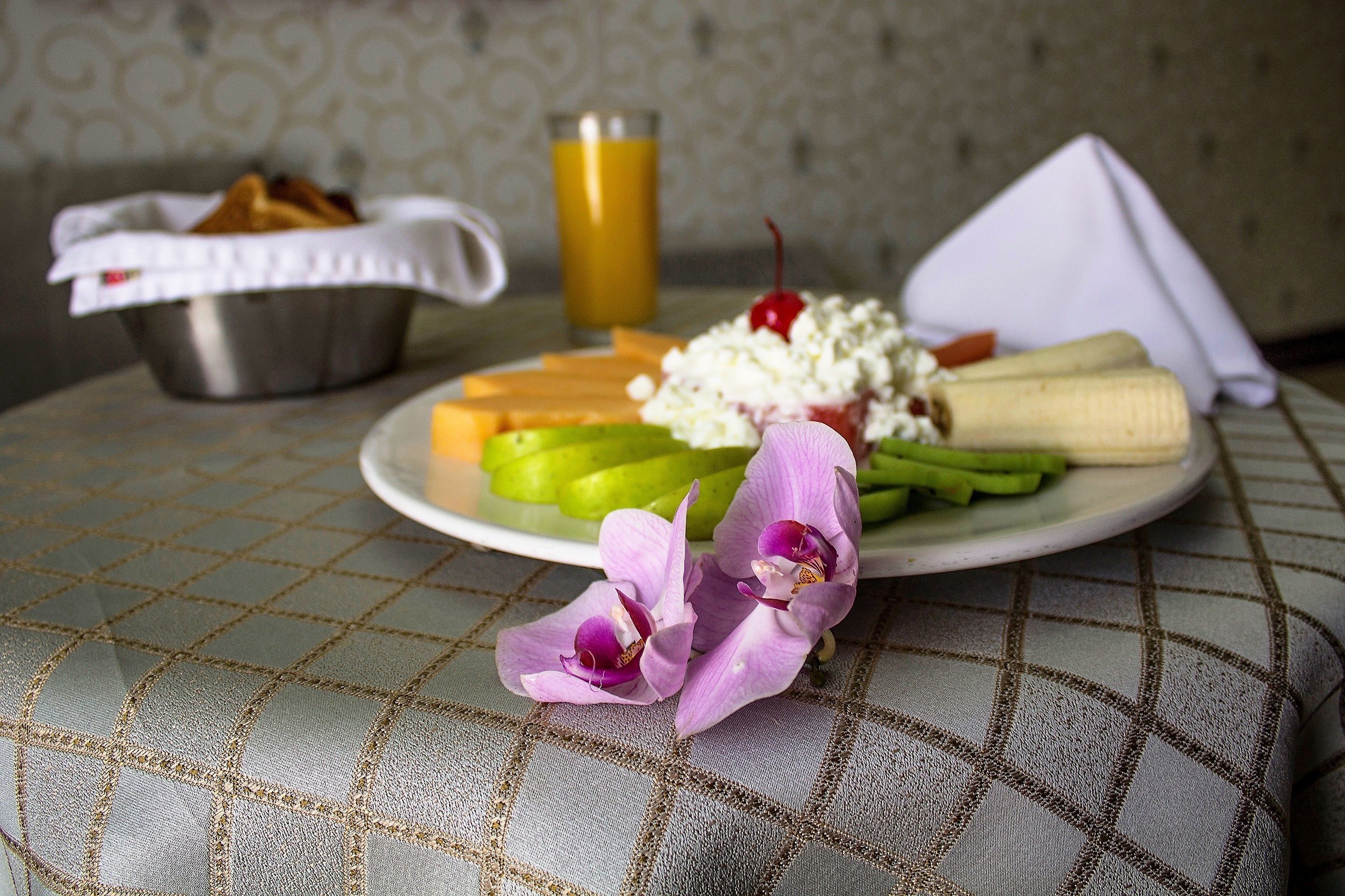 Une assiette contenant des aliments, un verre de jus d’orange et une serviette sur une table recouverte d’une nappe à motifs.