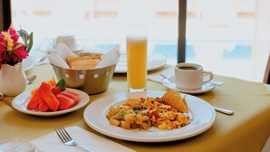 Una mesa de desayuno con huevos revueltos, tostadas, fruta, un vaso de jugo de naranja y una taza de café.