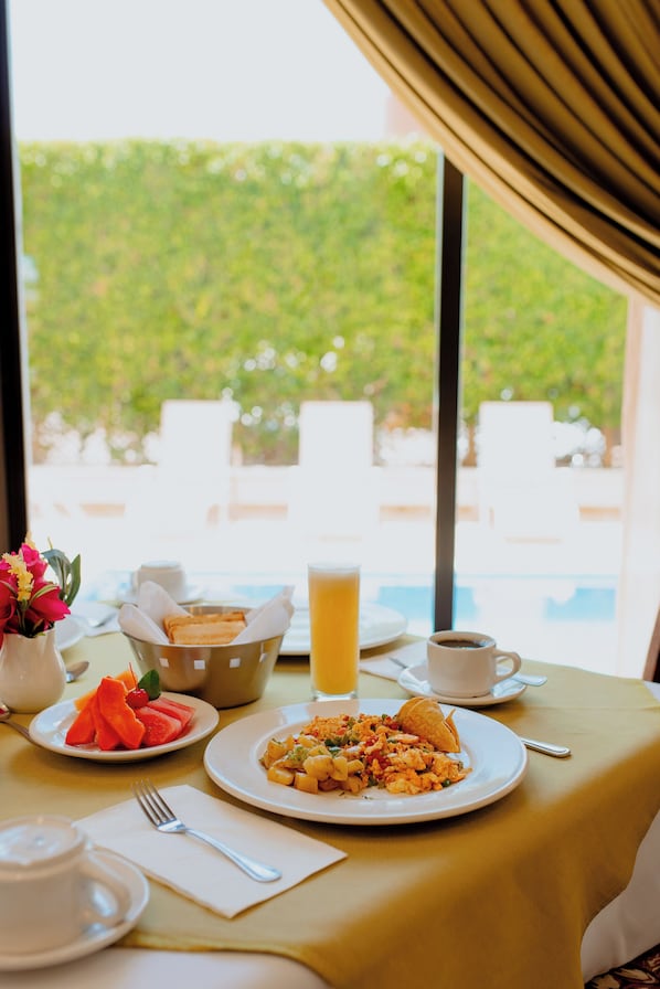 Una mesa de desayuno con huevos revueltos, tostadas, fruta, un vaso de jugo de naranja y una taza de café.