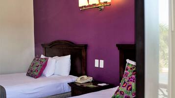 Une chambre d’hôtel avec deux lits, des murs violets et une table de chevet avec une lampe.
