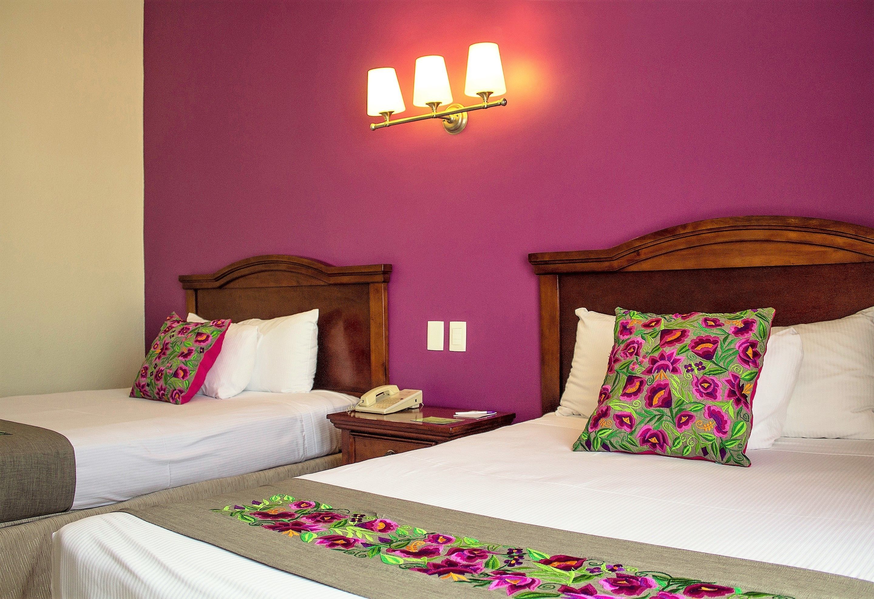 Una habitación de hotel con dos camas, un cabecero de madera, un teléfono en la mesita de noche y una pared morada.