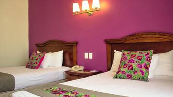 Una habitación de hotel con dos camas, un cabecero de madera, un teléfono en la mesita de noche y una pared morada.