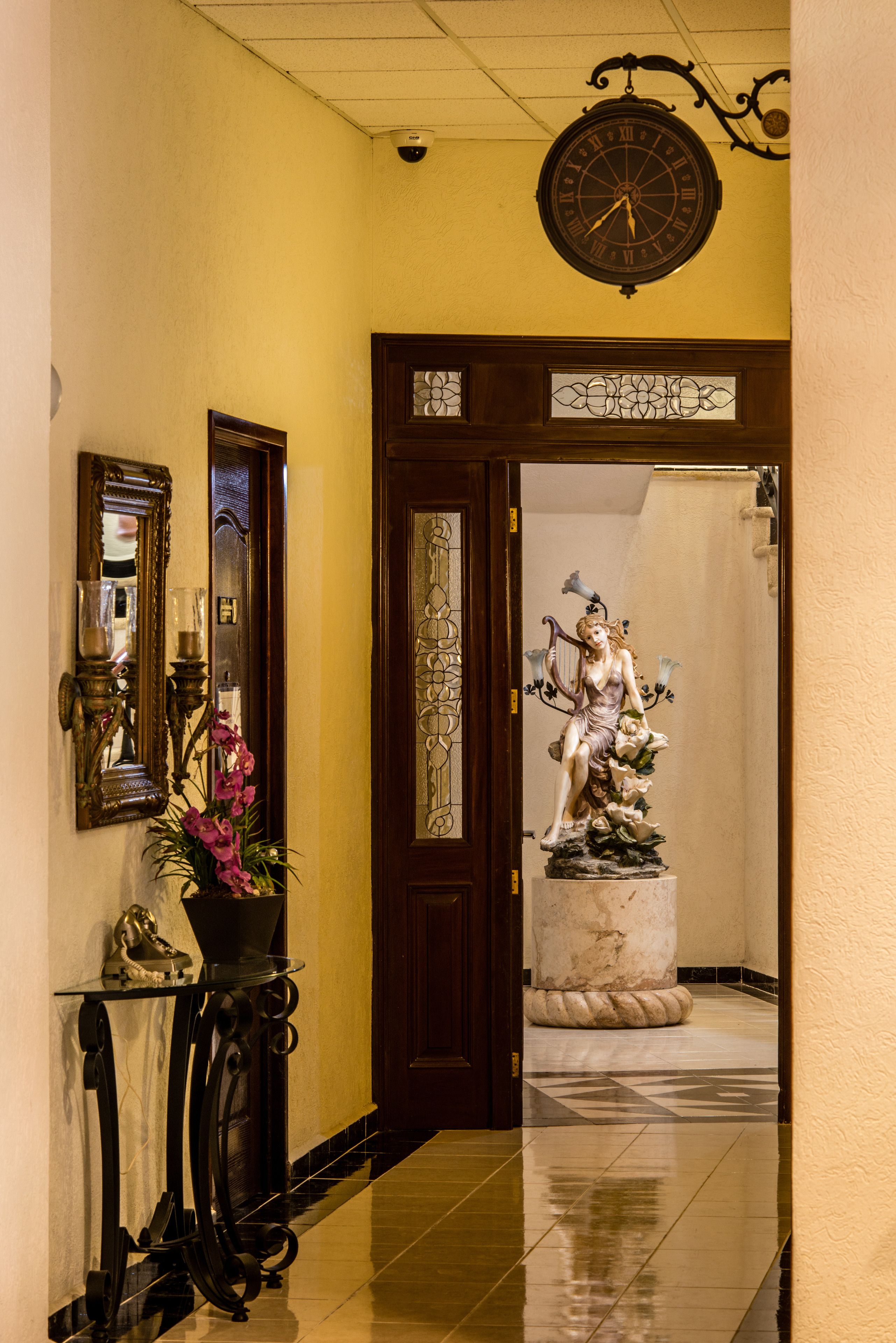 A hallway with a large clock, a statue, and a mirror.