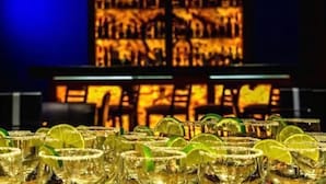 Una zona de bar con varios vasos de una bebida, probablemente un cóctel, adornada con rodajas de lima.