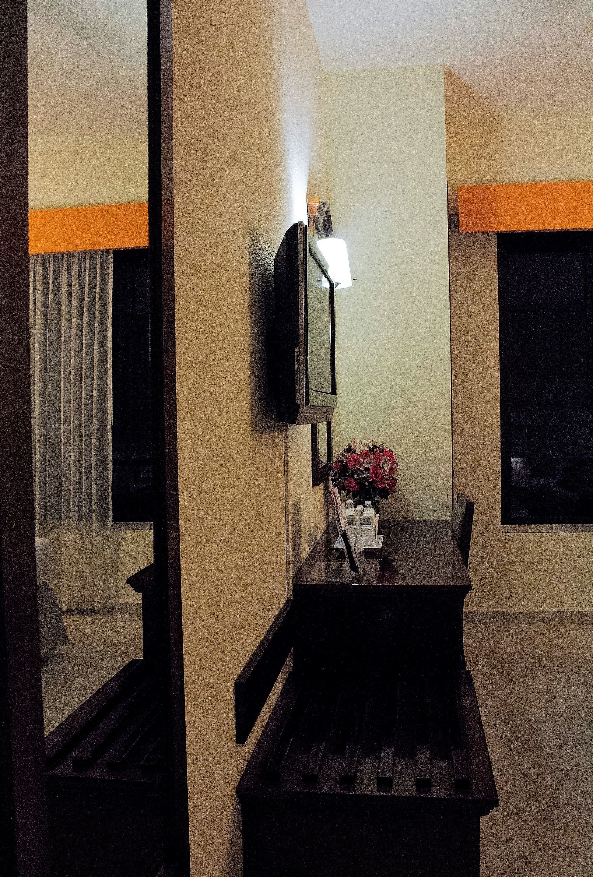Une chambre d’hôtel avec un lit, un bureau doté d’une lampe, un téléviseur fixé au mur et une fenêtre avec des rideaux.
