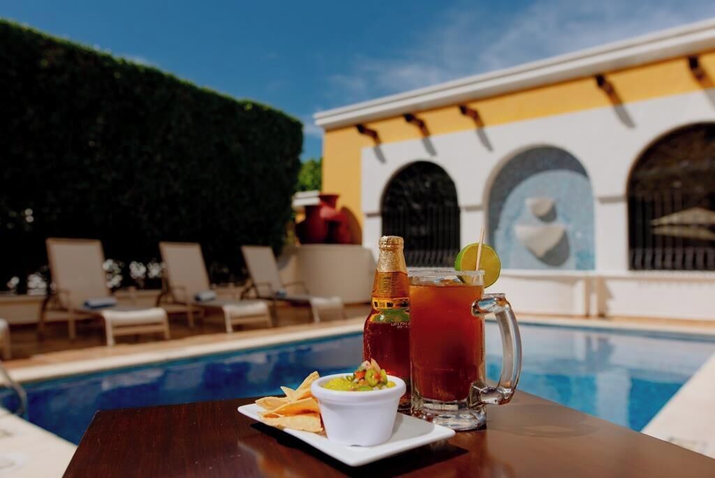 A poolside table with a cocktail, a bottle, and a small bowl of chips.