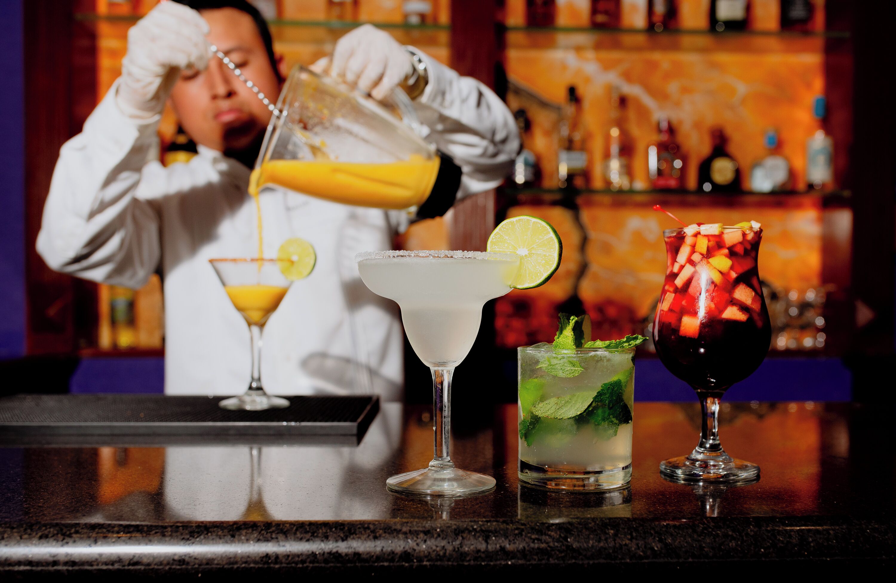 Un barman verse une boisson dans un verre à martini, et trois autres boissons sont posées sur le comptoir.