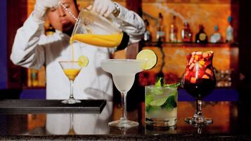 Un barman verse une boisson dans un verre à martini, et trois autres boissons sont posées sur le comptoir.