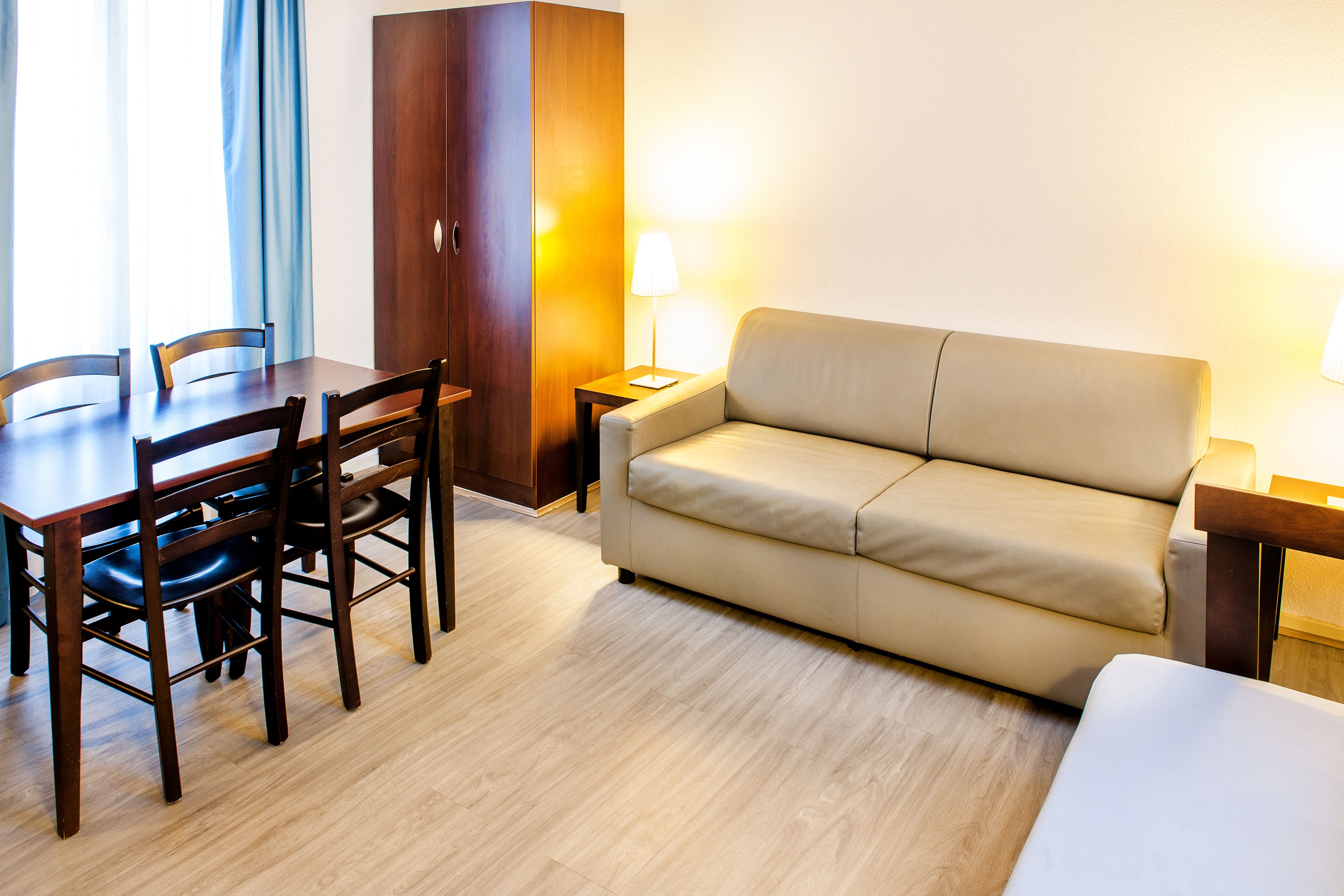 Ein Hotelzimmer mit einem Holztisch, vier Stühlen, einem beigen Sofa und zwei Nachttischlampen.