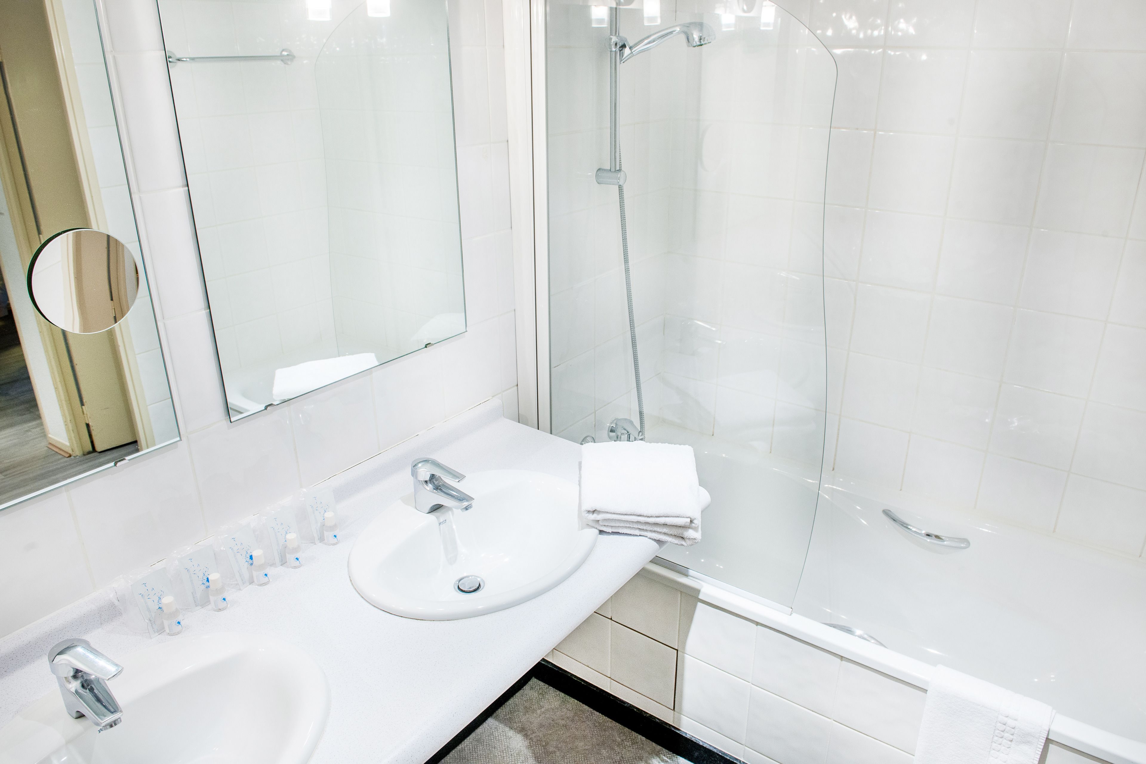 A modern bathroom with a glass-enclosed shower, a sink with a mirror, and neatly arranged toiletries.