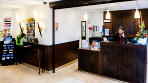A reception area with a wooden reception desk, a bulletin board, a vending machine, and a potted plant. - Appart'hôtel Saint Jean (Lourdes)