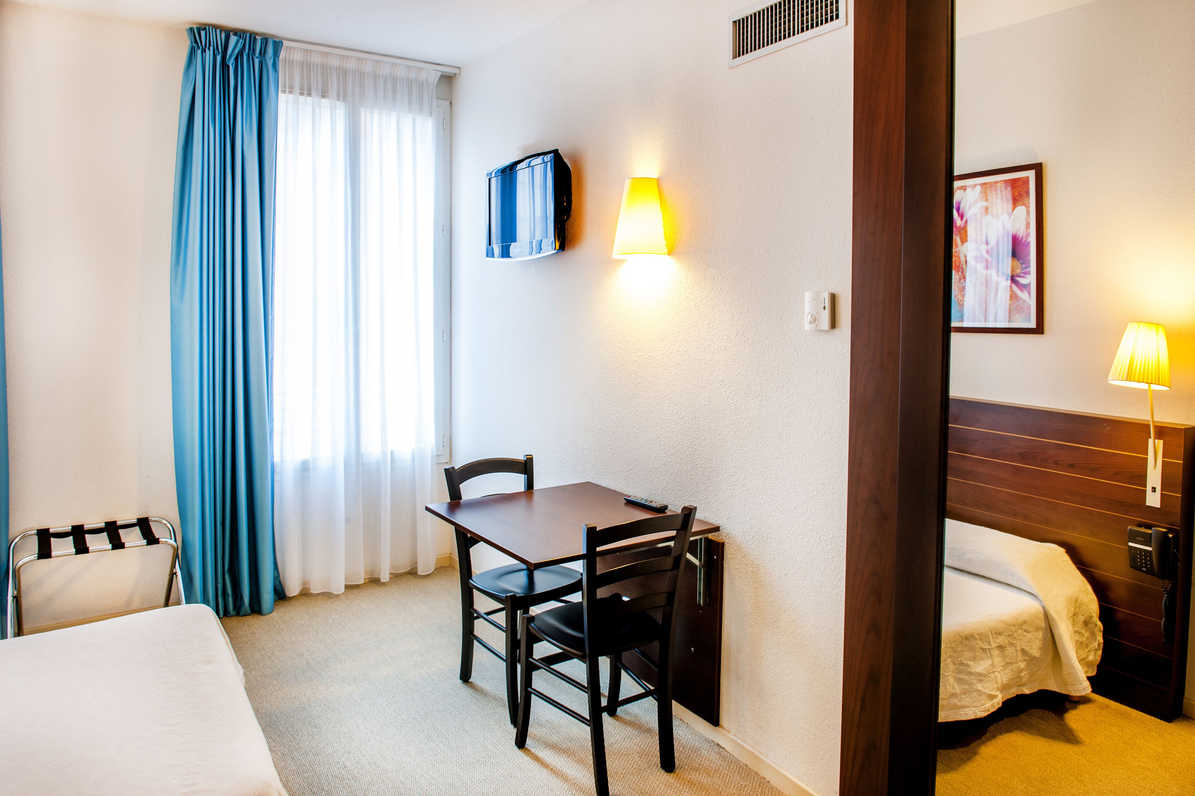 Habitación de hotel con cama, escritorio con silla, teléfono y televisor instalado en la pared.