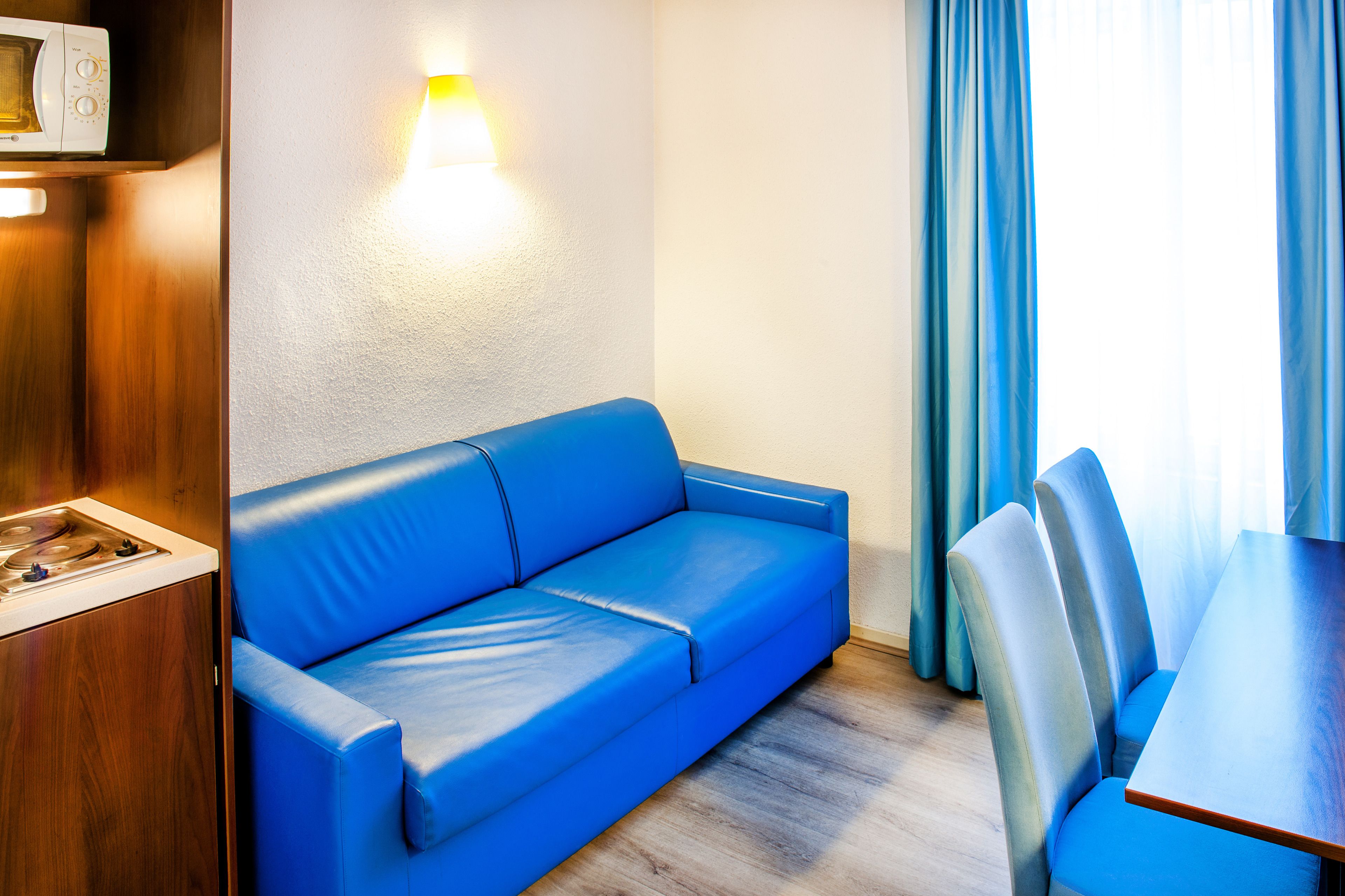 A compact room with a blue sofa, a wooden table, and a microwave on a shelf.
