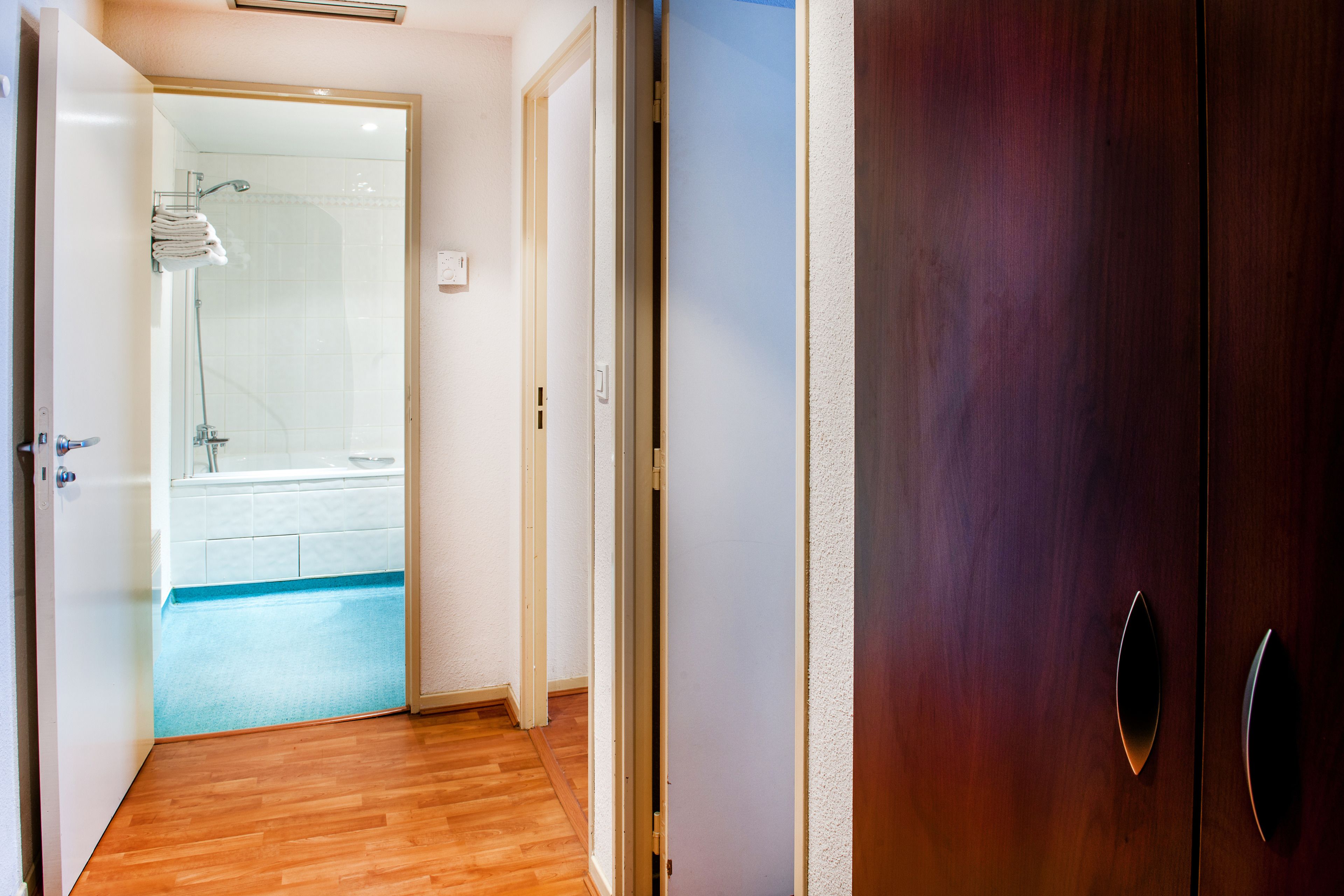 Un corridoio con pavimento in legno che conduce a un bagno con cabina doccia in vetro.