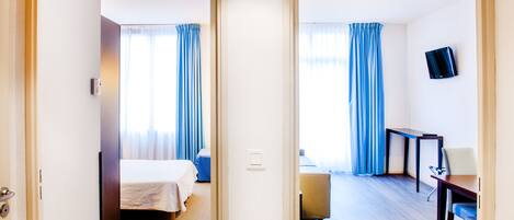 Een hotelkamer met een bed, een bureau, een stoel en een televisie aan de muur.