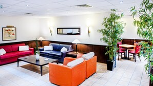A hotel lobby with a red sofa, blue sofa, orange sofa, and a wooden table. There are potted plants and a painting on the wall. - Appart'hôtel Saint Jean (Lourdes)