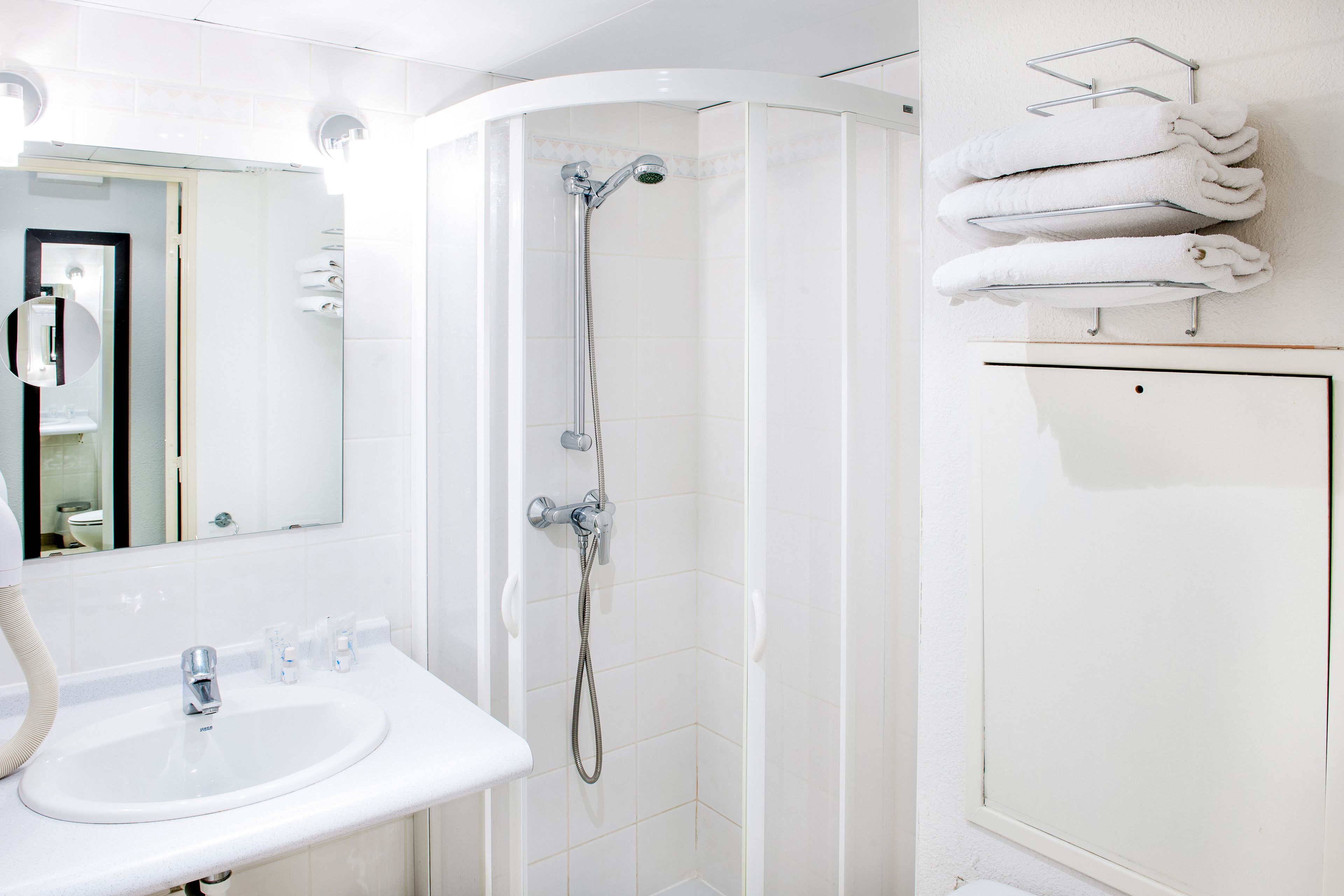 A modern bathroom with a white sink, a mirror, a shower with a handheld showerhead, and a towel rack with folded towels.