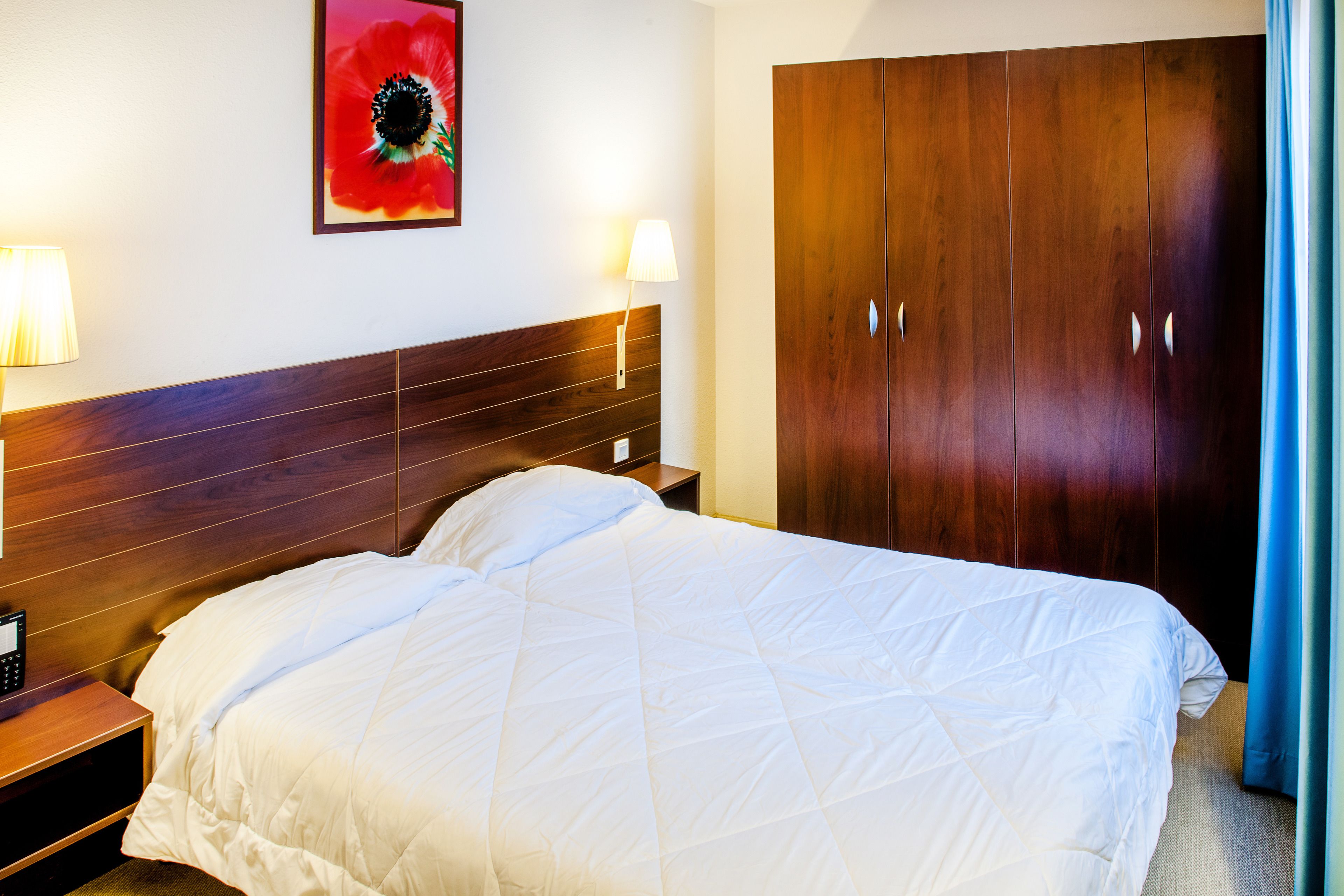 A hotel room with a large bed, wooden headboard, bedside lamps, and a wardrobe.
