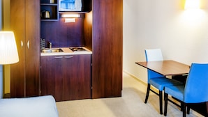 A compact hotel room with a kitchenette, a dining area with a table and chairs, and a bed. - Appart'hôtel Saint Jean (Lourdes)