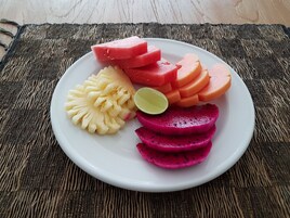 Uma travessa com melancia, abacaxi, pitaya e limão sobre um tapete tecido.