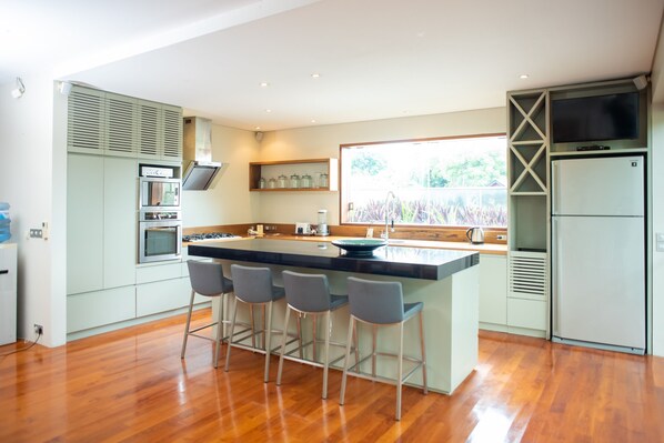 A modern kitchen with a central island, bar stools, built-in appliances, and a large window providing natural light.