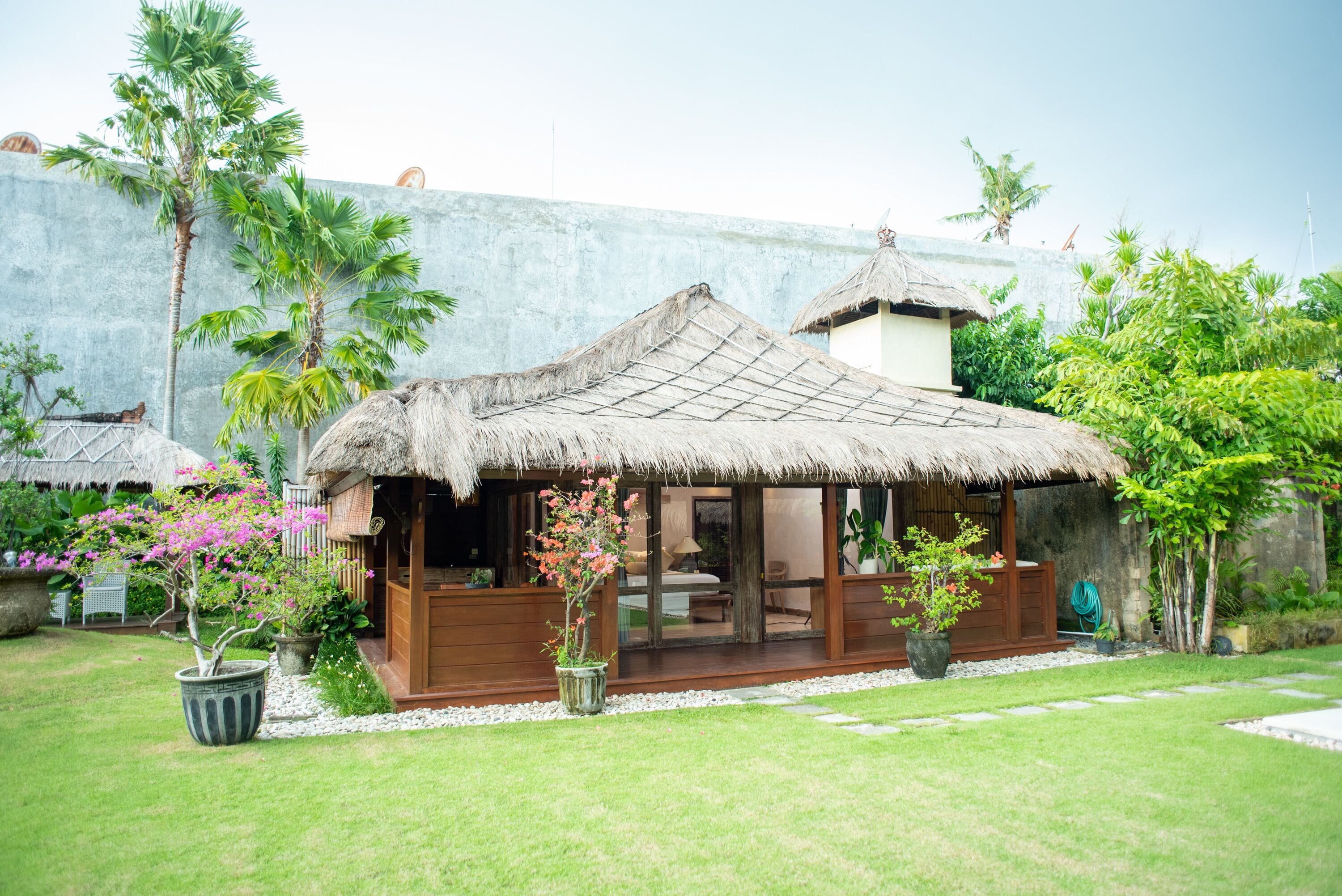 A thatched-roof structure with a wooden deck, surrounded by lush greenery and potted plants.