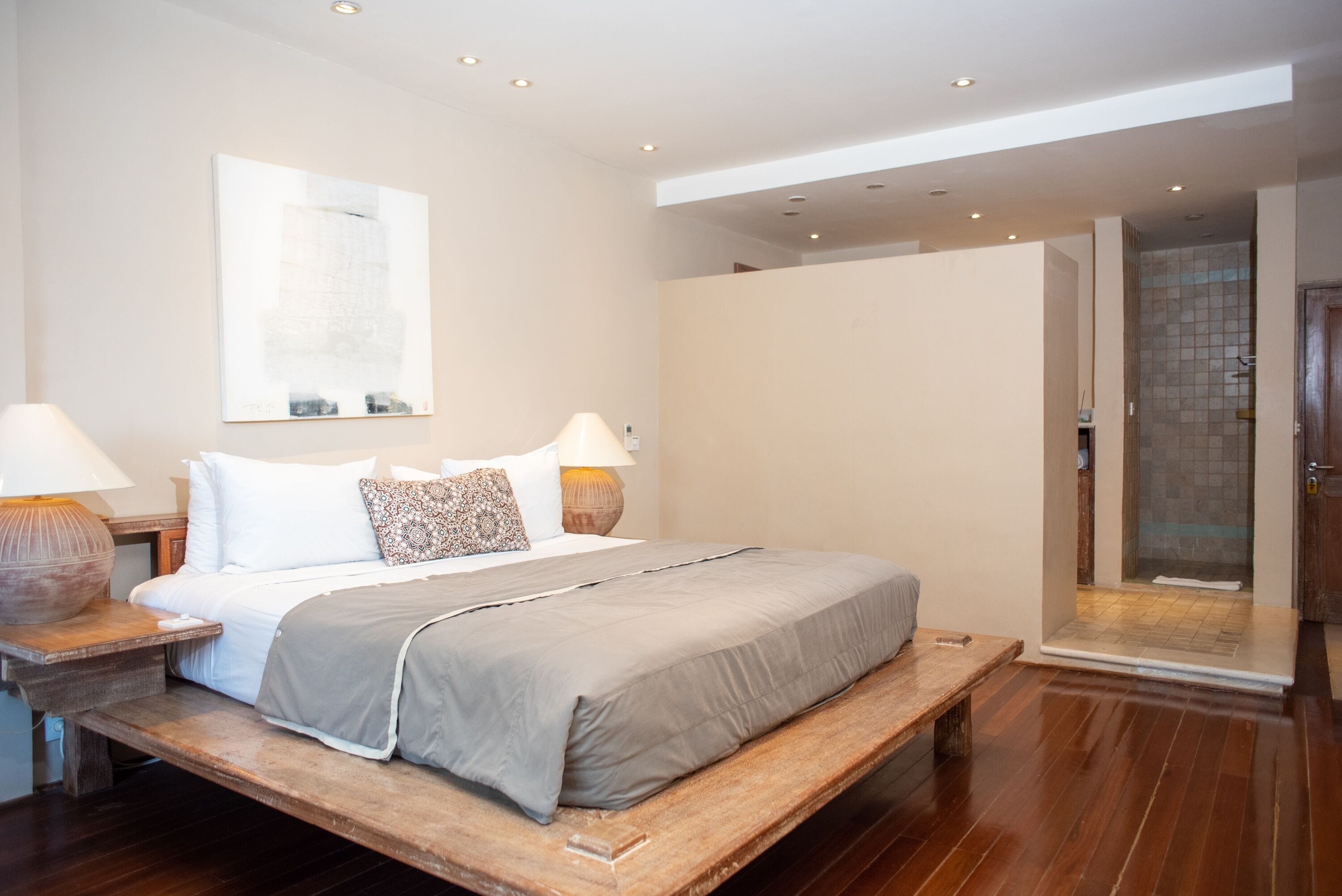 Une chambre moderne avec un grand lit, des lampes de chevet, un banc en bois et un espace douche.
