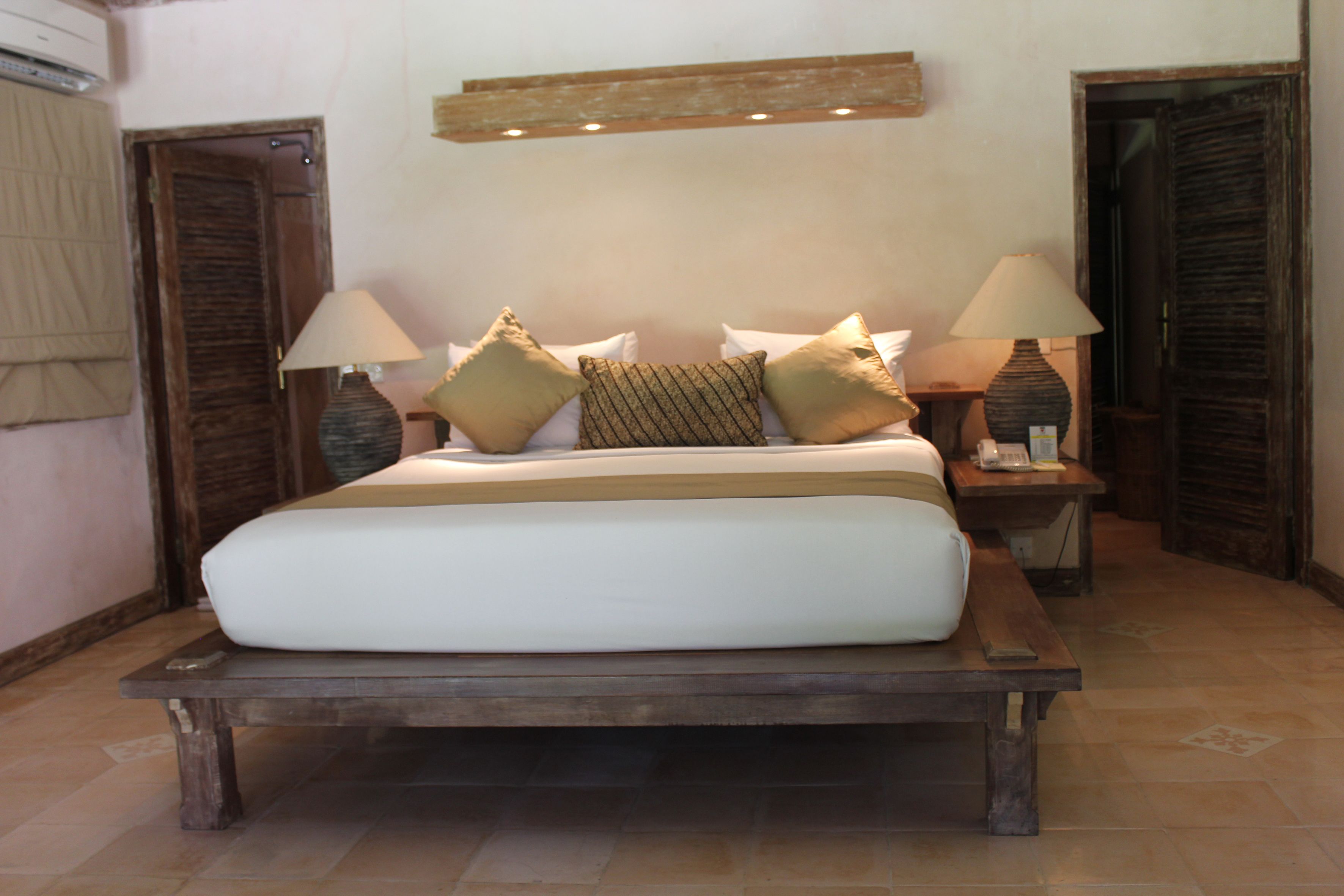 Una cama con estructura de madera, dos mesitas de noche con lámparas y una lámpara de pared sobre la cama.