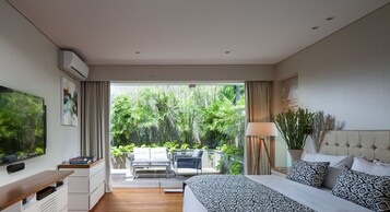 Quarto de hotel moderno com uma cama grande, televisão, escrivaninha e varanda com plantas.