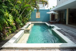 A rectangular pool with a stone border, surrounded by lush tropical plants and a wooden deck. - Sienna Villas Seminyak (Seminyak)