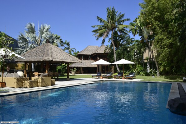 A pool area with lounge chairs, umbrellas, and thatched-roof structures. - Sienna Villas Seminyak (Seminyak)