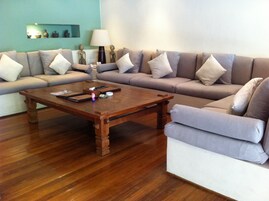 Uma sala de estar com mesa de centro de madeira, sofá bege e parede verde-água.