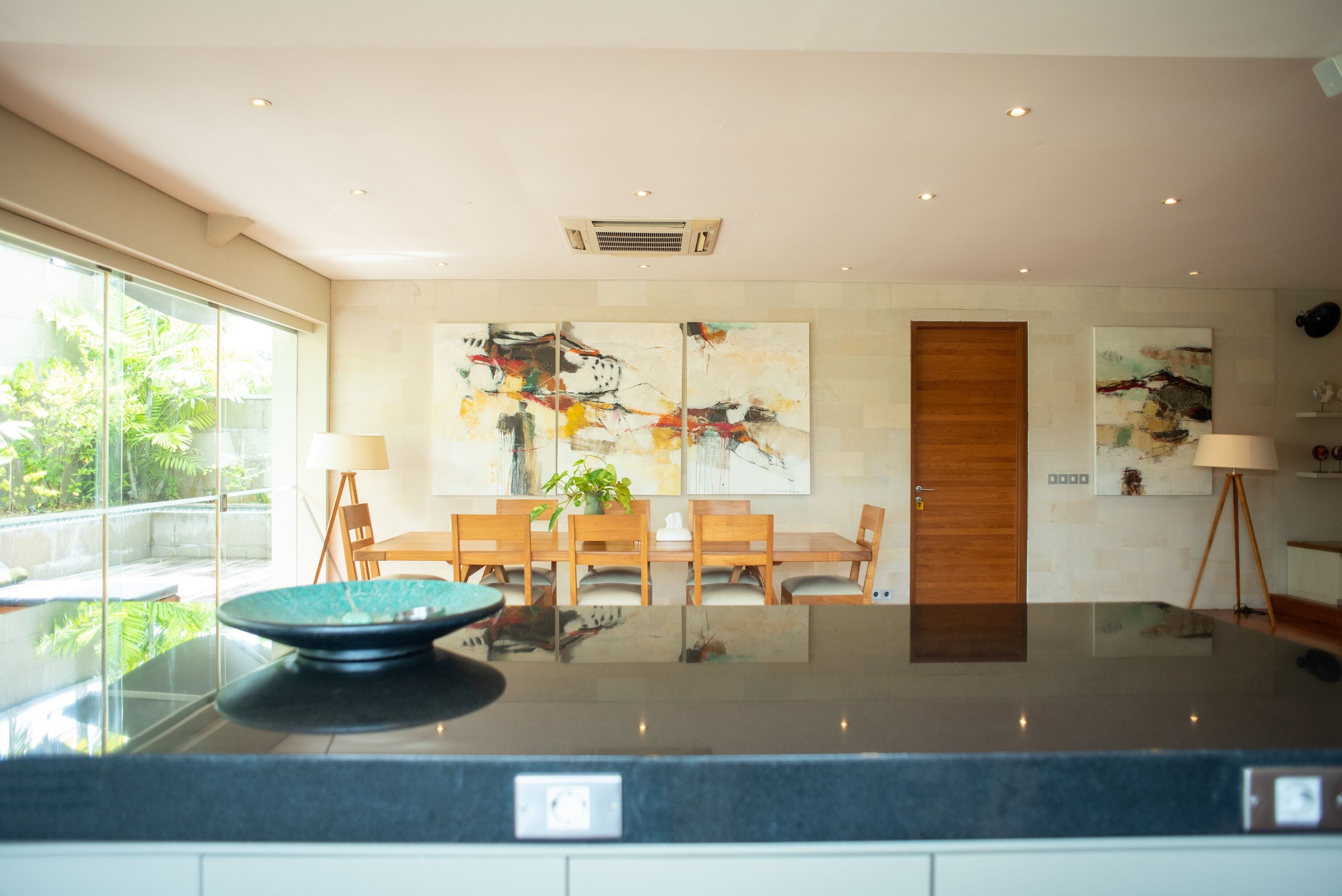 A modern dining area with a glass partition, wooden furniture, and abstract wall art.