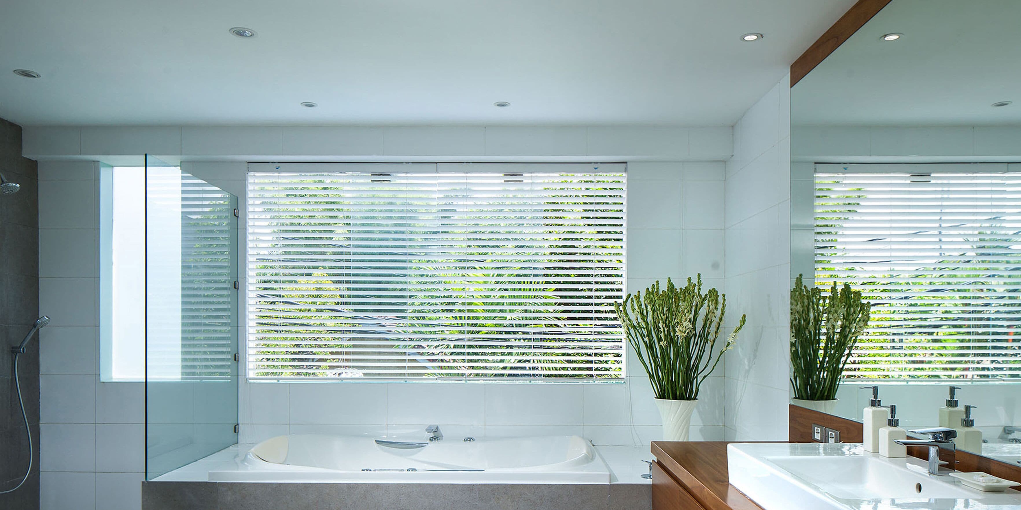 A modern bathroom with a glass-enclosed shower, a freestanding bathtub, and a large window with blinds.